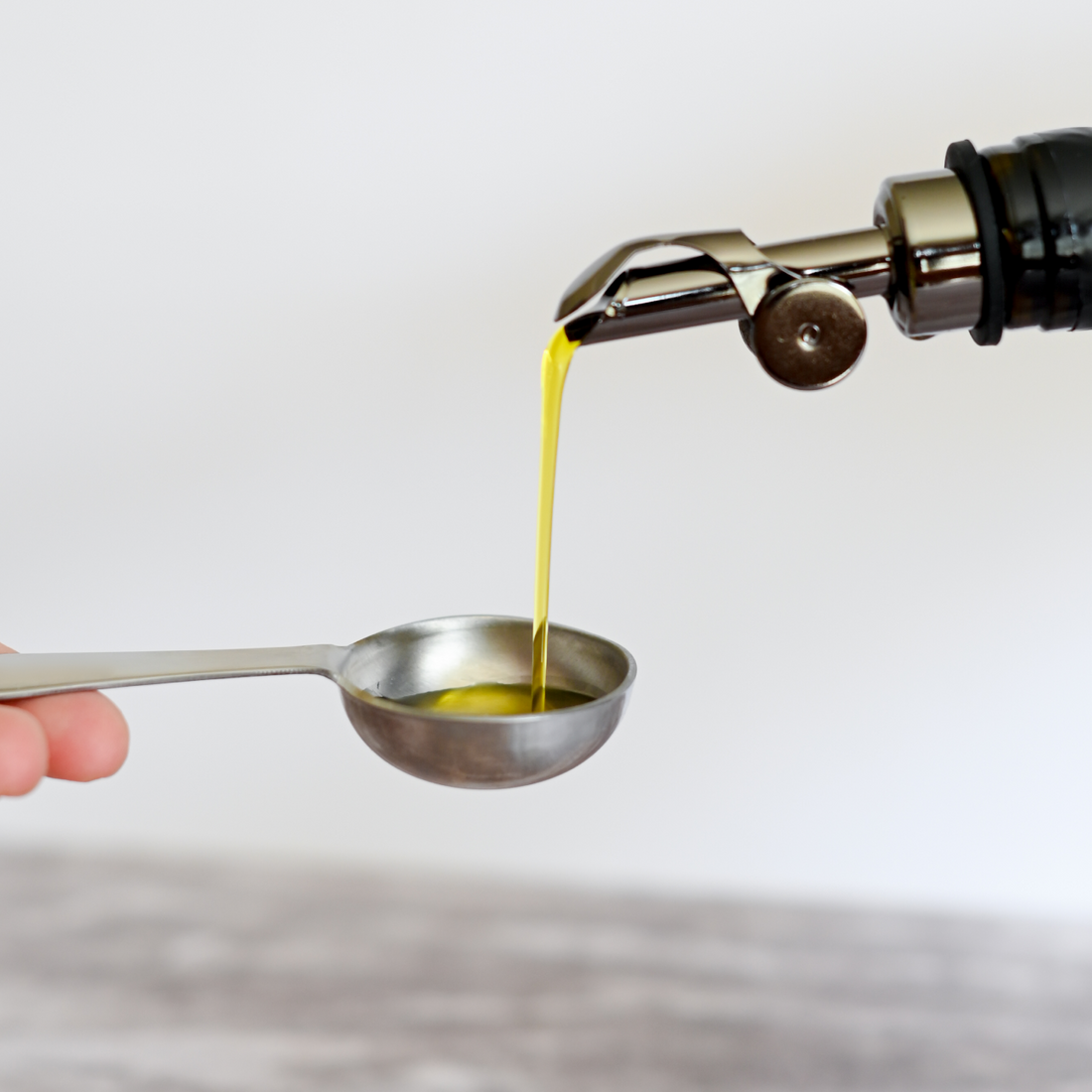 pouring extra virgin olive oil into a measuring spoon